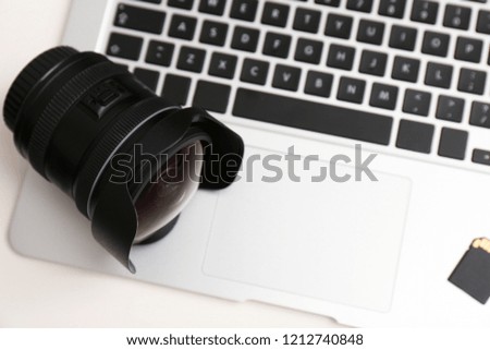 Camera lens on laptop, closeup. Professional photographer's equipment