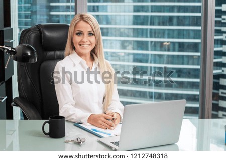Beautiful young girl woman office employee manager sits at a table with a laptop in an office in a skyscraper with a big city.