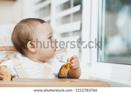 A child in a high chair eating a cracker with raisins
