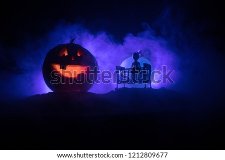 Horror Halloween concept. Old creepy eerie wooden baby crib and scary smiling glowing pumpkin in dark toned foggy background. Selective focus