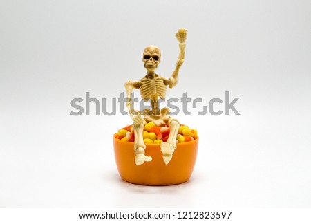 Halloween skeleton sitting on top of an orange bowl of candy corn isolated on a solid background