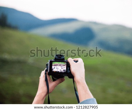 Hands holding the digital photo camera. Looking at the camera preview. Checking the playback screen. Mountain landscape in the background.