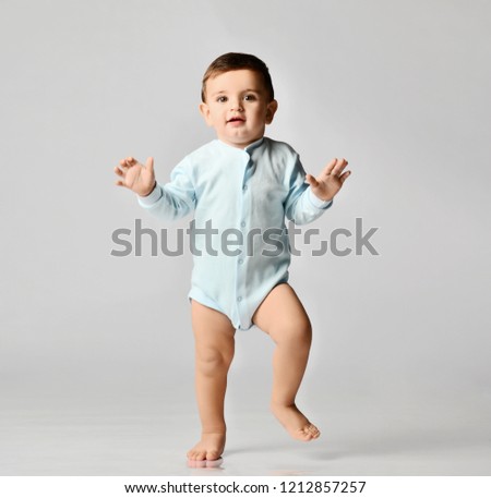 Infant child baby boy kid toddler in light blue body cloth make first steps on grey  background