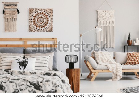 Warm ethno bedroom with patterned pillows on the bed and couch and macrame on the wall, real photo Royalty-Free Stock Photo #1212876568
