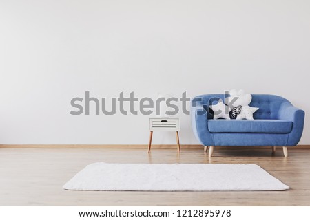White carpet, blue sofa and cute pillows in elegant child's room with posters on the wall, real photo