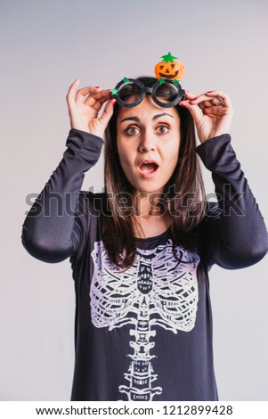 young woman wearing funny halloween glasses and smiling. White background. LIfestyle indoors. Skeleton costume