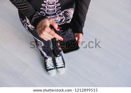top view of a young woman using mobile phone. Wearing a black and white skeleton costume. Halloween concept. Indoors. Technology