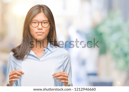 Young asian woman over isolated background holding blank paper with a confident expression on smart face thinking serious