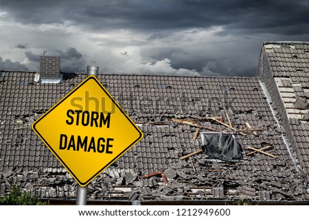 yellow damage warning sign in front of roof of house damaged by heavy hurricane tornado storm Royalty-Free Stock Photo #1212949600