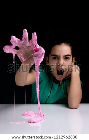 Adorable girl holding and playing with a pink slime. She is having fun and making faces. Black background with copyspace.
