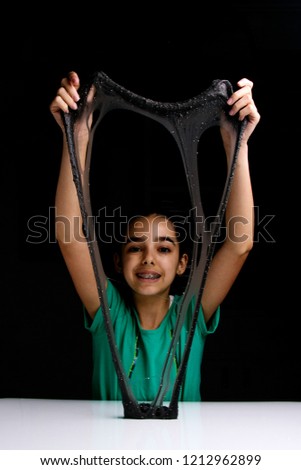 Cute girl playing with a black glitter slime. She is having fun and making faces. Black background with copyspace.
