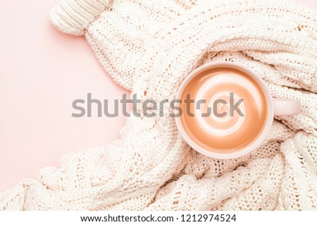 A cup of aromatic coffee with cream and a warm sweater on a pink background. Close up