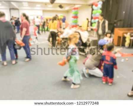 Motion blurred kids and parents with strollers enjoy indoor Halloween party at school in Texas, America. Defocused children with costumes at fall fun games