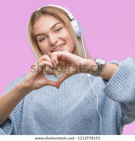 Young caucasian woman listening to music wearing headphones over isolated background smiling in love showing heart symbol and shape with hands. Romantic concept.
