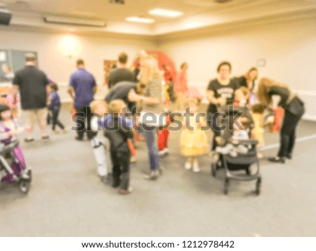 Motion blurred kids and parents with strollers enjoy indoor Halloween party at school in Texas, America. Defocused children with costumes at fall fun games