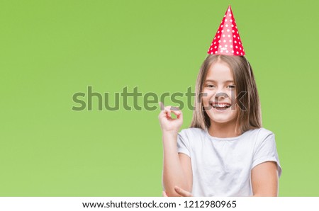 Young beautiful girl wearing birthday cap over isolated background with a big smile on face, pointing with hand and finger to the side looking at the camera.