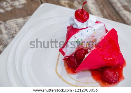 Strawberry cold crepe cake with cherry in white dish on wooden table.