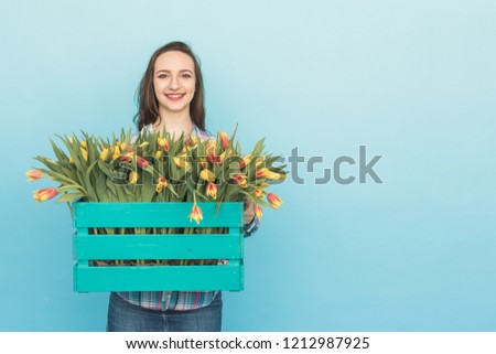 Happy caucasian young woman with box of yellow tulips on blue background