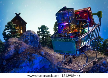 Shopping cart with Christmas presents at winter nature background with mountains, fir-trees and house. Christmas and New Year composition.