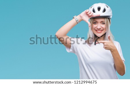 Young blonde woman wearing cyclist security helmet over isolated background smiling making frame with hands and fingers with happy face. Creativity and photography concept.