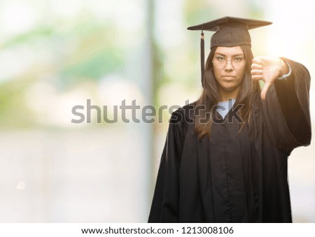 Young hispanic woman wearing graduated cap and uniform looking unhappy and angry showing rejection and negative with thumbs down gesture. Bad expression.