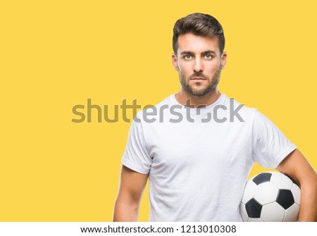 Young handsome man holding soccer football ball over isolated background with a confident expression on smart face thinking serious
