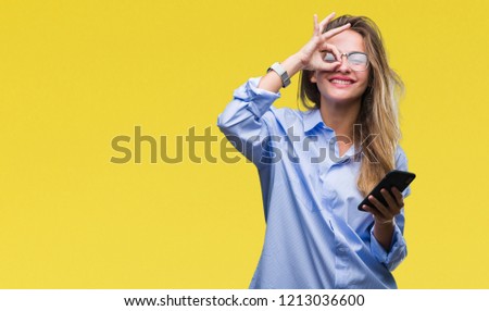 Young beautiful blonde business woman using smartphone over isolated background with happy face smiling doing ok sign with hand on eye looking through fingers