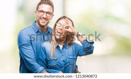 Young couple in love wearing glasses over isolated background doing ok gesture with hand smiling, eye looking through fingers with happy face.