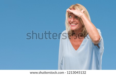 Middle age blonde business woman over isolated background very happy and smiling looking far away with hand over head. Searching concept.