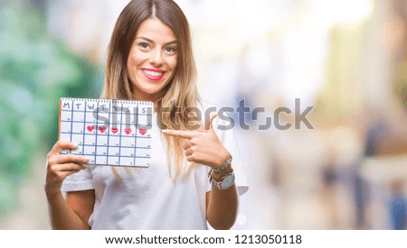 Young beautiful woman holding menstruation calendar over isolated background very happy pointing with hand and finger