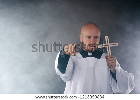 Catholic priest exorcist in white surplice and black shirt with cleric collar praying with crucifix Royalty-Free Stock Photo #1213050634