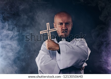 Catholic priest exorcist in white surplice and black shirt with cleric collar praying with crucifix Royalty-Free Stock Photo #1213050640