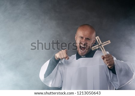 Catholic priest exorcist in white surplice and black shirt with cleric collar praying with crucifix Royalty-Free Stock Photo #1213050643