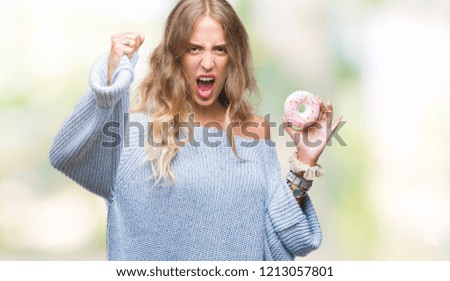 Beautiful young blonde woman eating pink donut over isolated background annoyed and frustrated shouting with anger, crazy and yelling with raised hand, anger concept