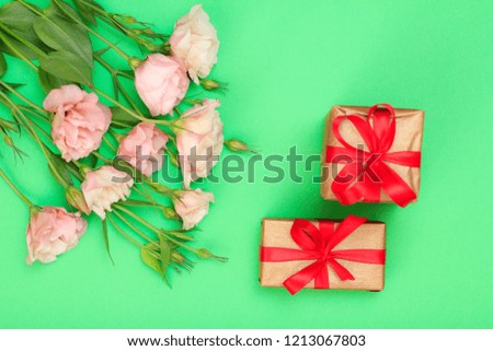Bouquet of pink flowers with leaves and two gift boxes on green background. Top view. Celebration day concept.