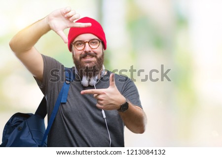 Young hipster man wearing red wool cap and backpack over isolated background smiling making frame with hands and fingers with happy face. Creativity and photography concept.