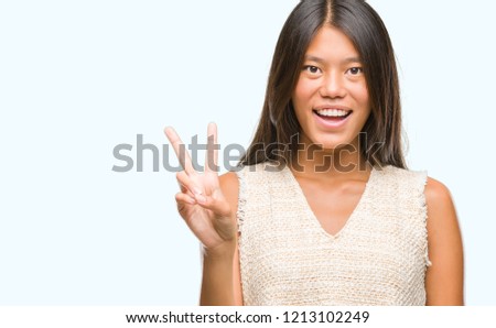 Young asian woman over isolated background smiling with happy face winking at the camera doing victory sign. Number two.