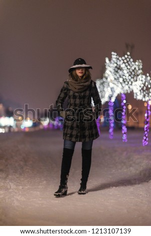 Young girl walking in front of trees decorated with colorful lights for Christmas night, blurred in the background