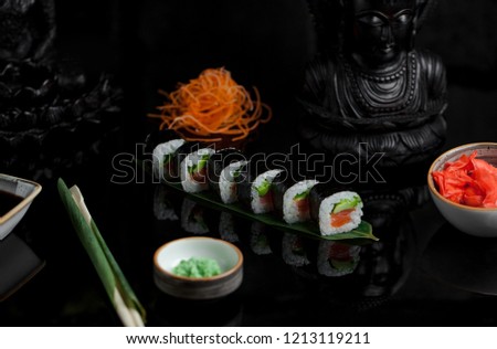 Sushi rolls on dark background with chopsticks and salmo, wasabi and vegetables on a plate. Japanese food.