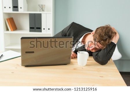 Joke, business people and humor concept - Tired businessman sleeping after hard working day in office interior. Man lying on table with laptop computer on.