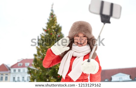 people, season and leisure concept - happy smiling woman in winter fur hat taking selfie by smartphone over christmas tree at tallinn old town hall square background