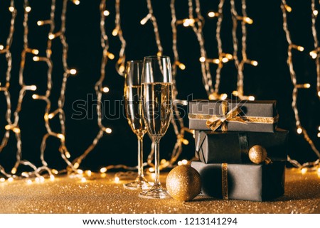christmas presents and glasses of champagne on garland light background