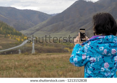 a girl in a warm jacket photographs on a smartphone autumn mountain landscape with a road