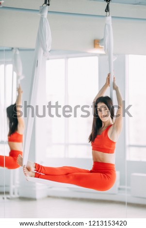 Training in the hall on a hammock. Yoga with a beautiful girl in red clothes.