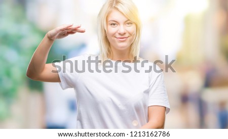 Young beautiful blonde woman wearing white t-shirt over isolated background gesturing with hands showing big and large size sign, measure symbol. Smiling looking at the camera. Measuring concept.