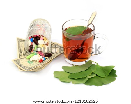 Strong herbal tea with ginko beloba leaves and a glass with pills on dollars