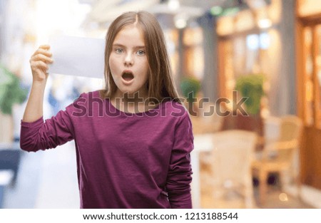 Young beautiful girl holding blank paper card over isolated background scared in shock with a surprise face, afraid and excited with fear expression