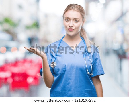 Young blonde surgeon doctor woman over isolated background smiling cheerful presenting and pointing with palm of hand looking at the camera.