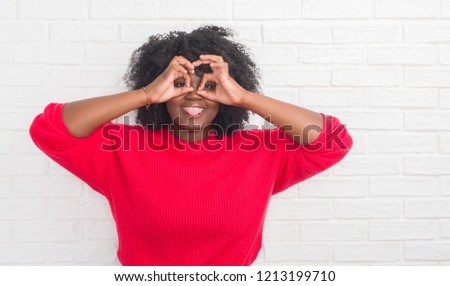 Young african american plus size woman over white brick wall doing ok gesture like binoculars sticking tongue out, eyes looking through fingers. Crazy expression.