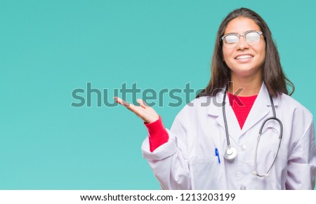 Young arab doctor woman over isolated background smiling cheerful presenting and pointing with palm of hand looking at the camera.
